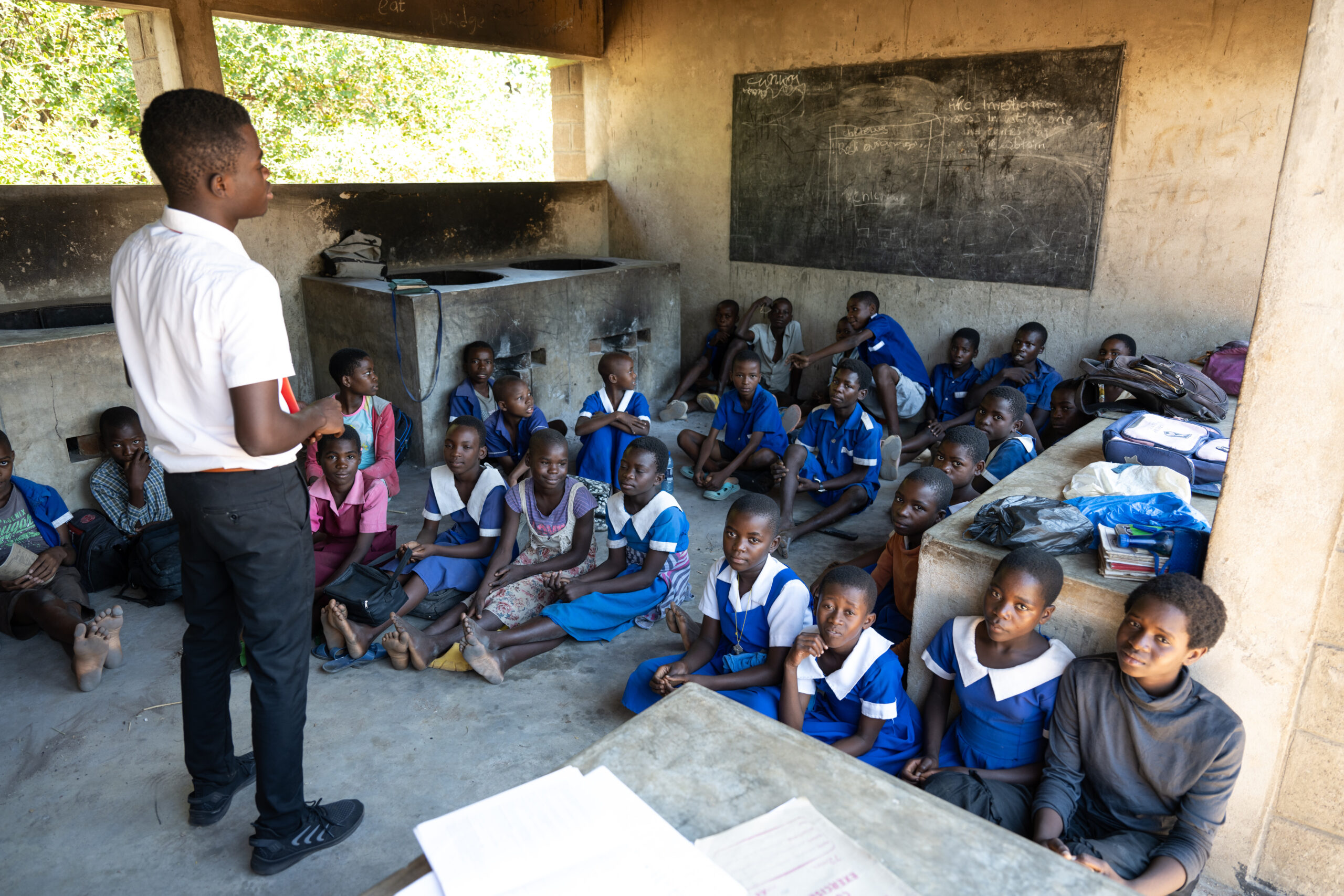 Schulkinder in Malawi am Boden sitzend, davor ein Lehrer