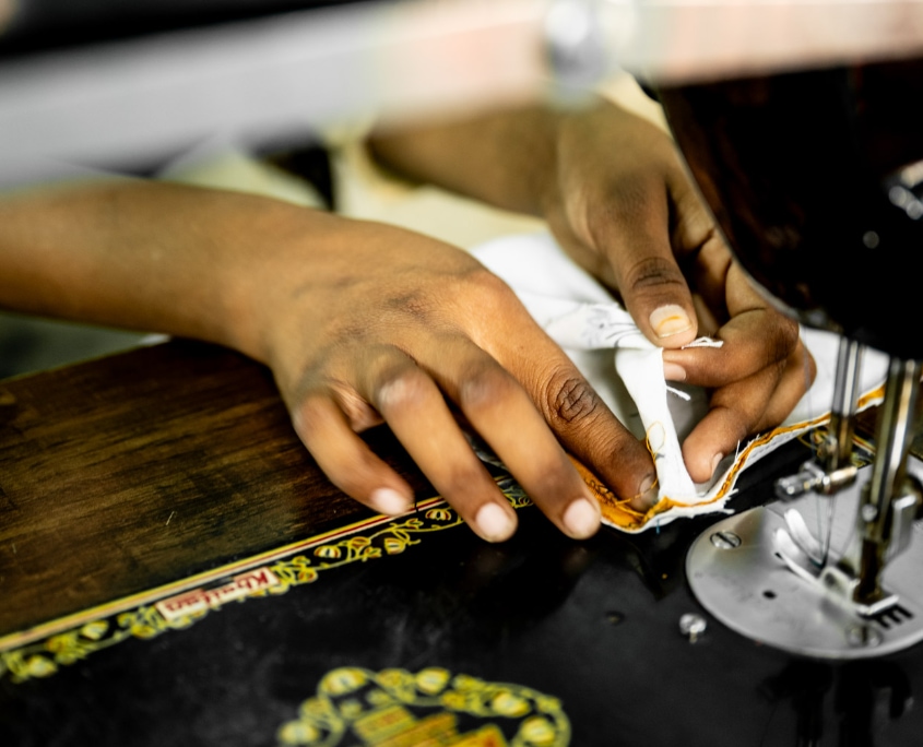 Hände einer Teilnehmerin nähen Stoff an einer Nähmaschine in der Schneiderausbildung in Bihar, Indien