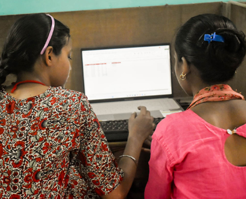 Indien-Computerkurs-2 Zwei Frauen sitzen in einem Computerkurs vor Bildschirmen. Man sieht sie von hinten.