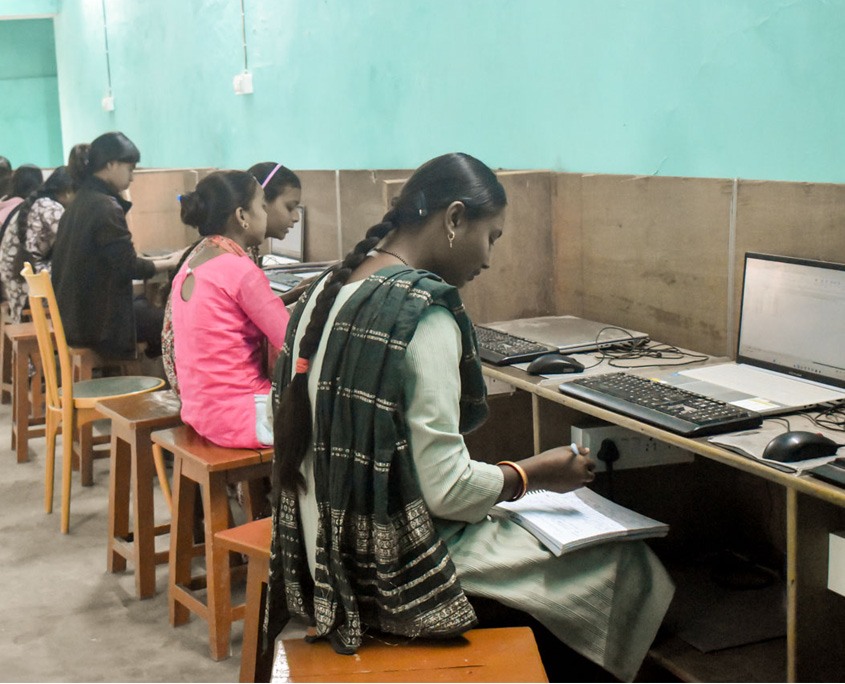 Indien-Computerkurs-4 Mehrere Frauen sitzen in einem Computerkurs vor Bildschirmen. Man sieht sie von der Seite