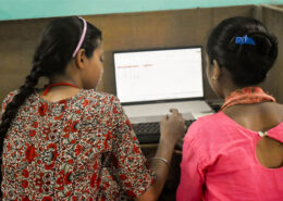 Zwei Frauen sitzen in einem Computerkurs vor Bildschirmen. Man sieht sie von hinten.