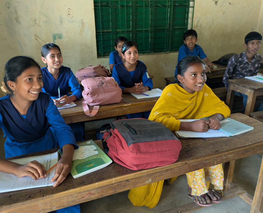 Blick ins Klassenzimmer. Schülerinnen und Schüler sitzen an Lernpulten und haben ihre Schulsachen vor sich aufgebreitet