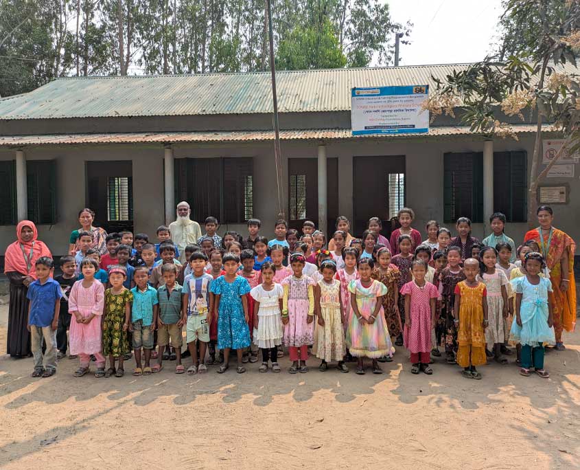 vor einer sonne dorfschule sind alle kinder versammelt, die sich zu einem gruppenbild aufstellen.