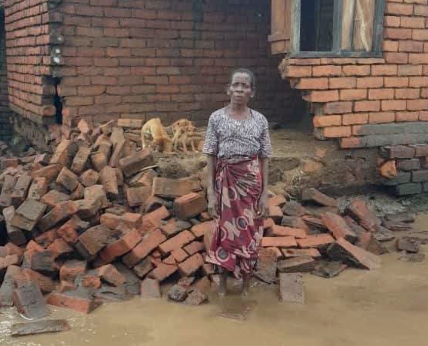 Nahaufnahme einer Frau vor ihrem stark beschädigten Haus nach Überschwemmung in Malawi, Trümmer und stehendes Wasser davor