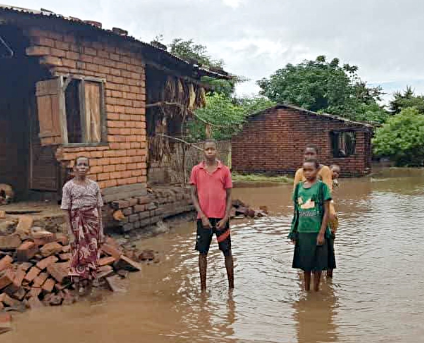 Menschen stehen knietief im Wasser vor ihrem zerstörten Haus in Malawi