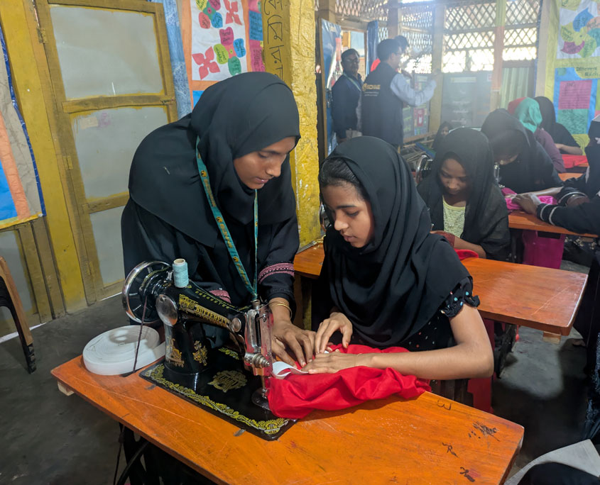 Eine Trainerin zeigt einer Schülerin an der Nähmaschine den nächsten Schritt. Bangladesch