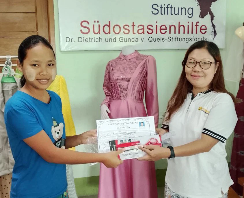 Zertifikatsübergabe_Beitragsslider SONNE Lehrerin übergibt einer Schülerin das Zertifikat für den Schneidereikurs in Yangon