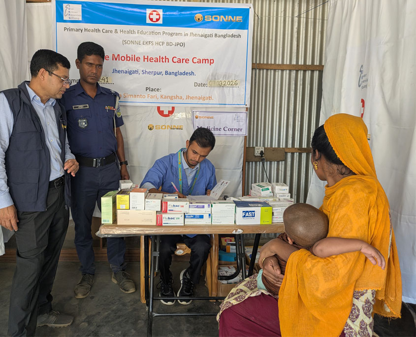 Blick in eine Sonne gesundheitsstation. im vordergrund eine Frau mit Baby im Arm. Sie sitzt vor der medikamentenausgabe, wo ein sonne-mitarbeiter ihr die medikamente aushändigt.