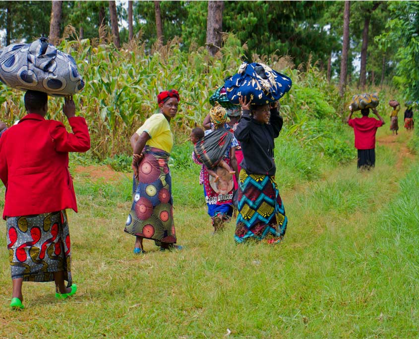 Malawi-Nothilfe-1 Mehrere Frauen tragen die erhaltenen Hilfsgüter nach Hause. Sie alle tragen bunte Röcke und balancieren die Hilfspakete auf dem Kopf.