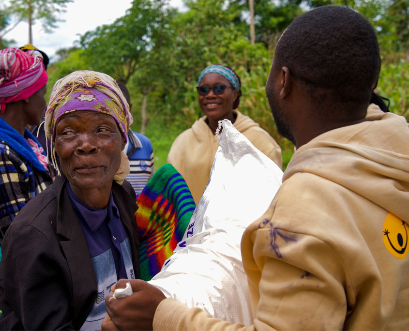 Malawi-Nothilfe-5 Eine Frau lacht und eine SONNE Mitarbeiterin überreicht ihr einen Sack Maismehl