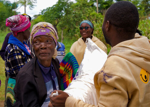 Eine Frau lächelt und eine SONNE Mitarbeiterin überreicht ihr einen Sack Maismehl